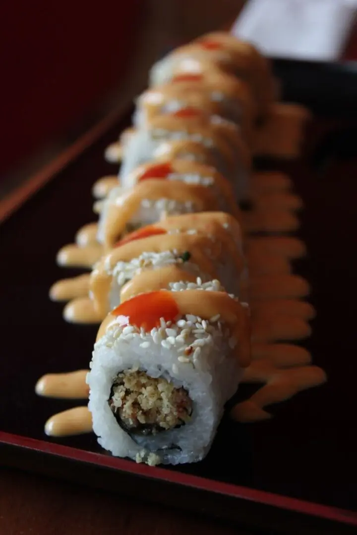 A sushi roll with sauce and rice on top of it.